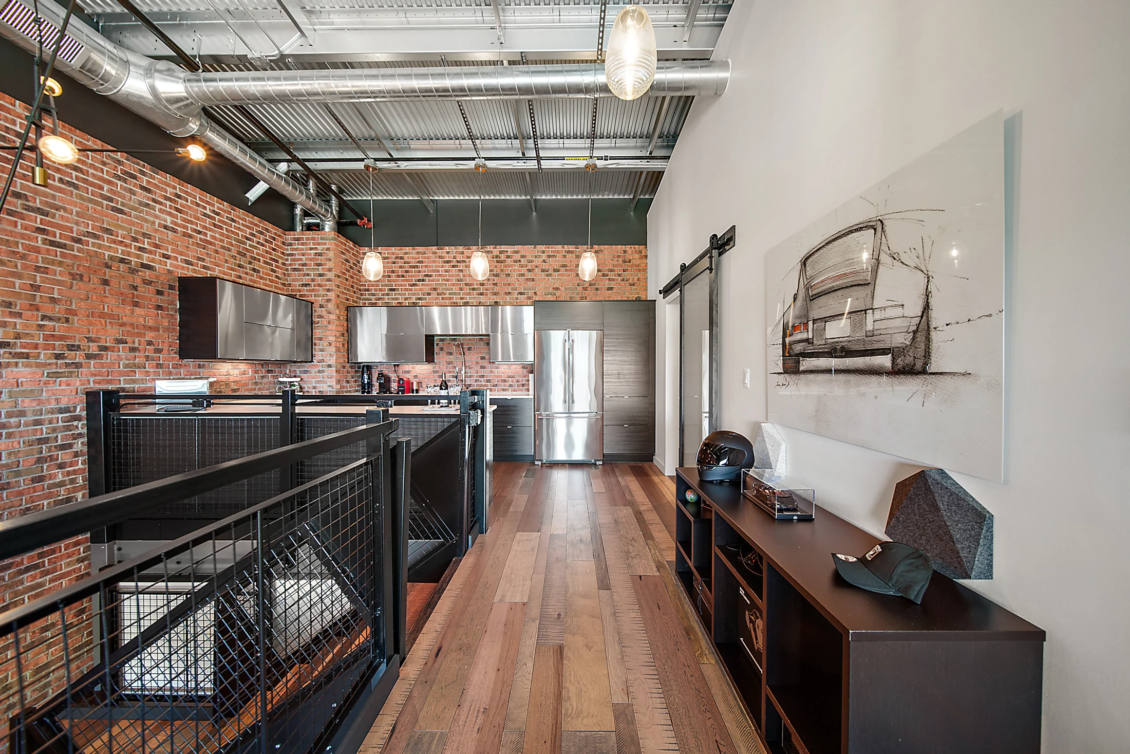 The mezzanine walkway, with a mesh railing, wood floor and a kitchen set against brick.