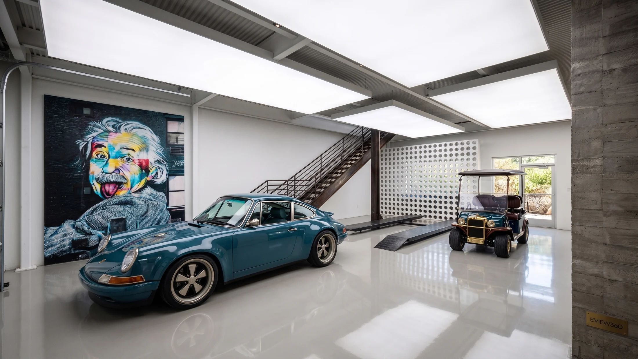 Unit 705 vehicle collection, with a blue sports car beneath skylights and a steel stair to the lounge.