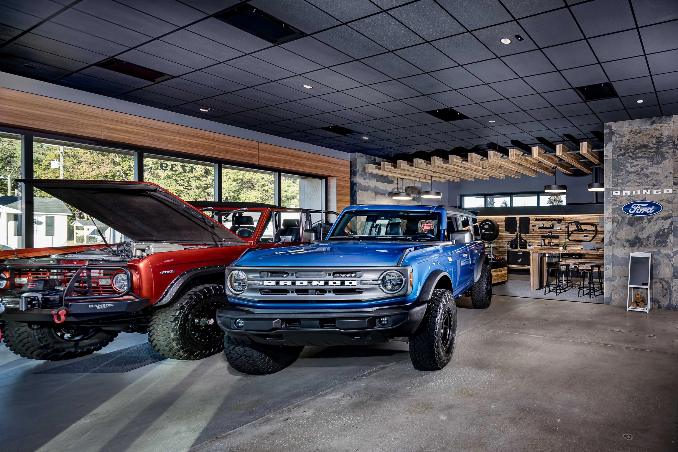 Ford Bronco showroom with vehicles beneath a timber-framed display and exposed black ceiling
