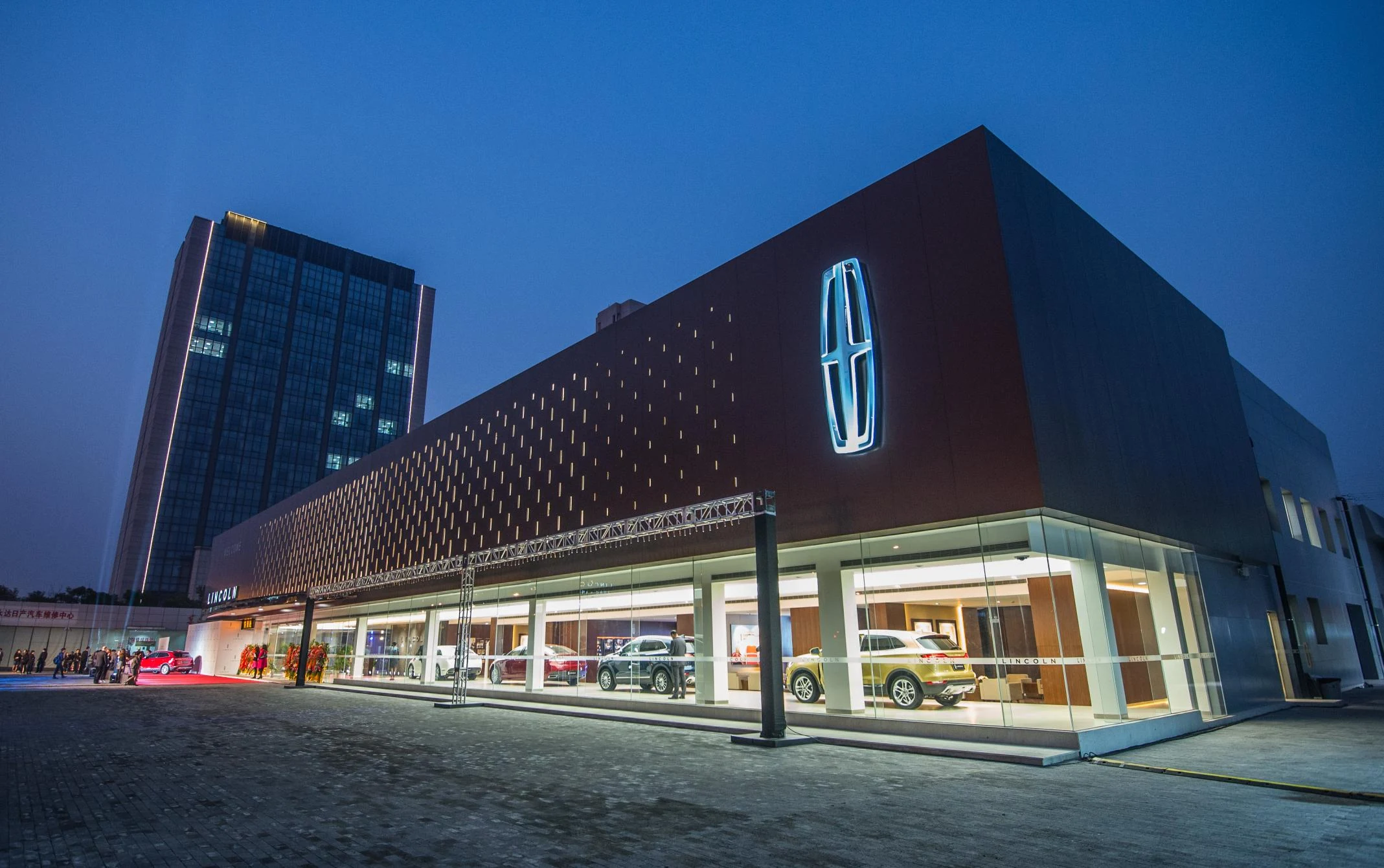 Lincoln of China retail flagship at dusk, with illuminated patterned facade and vehicles visible through the showroom